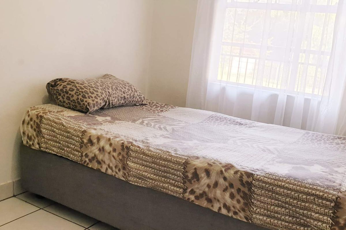 A simple bedroom featuring tiled flooring and a window with sheer curtains, providing natural light to the space.