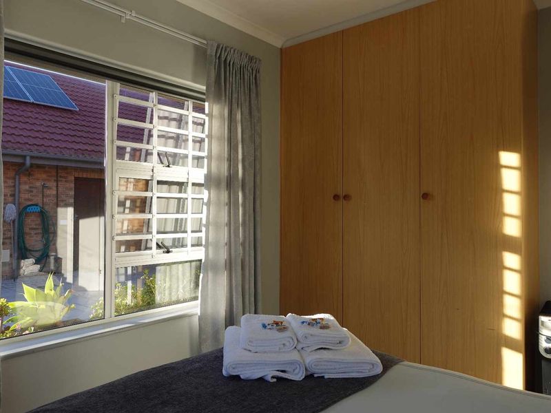 A bedroom featuring a built-in wooden wardrobe and a window with security bars, offering a view of the exterior area.