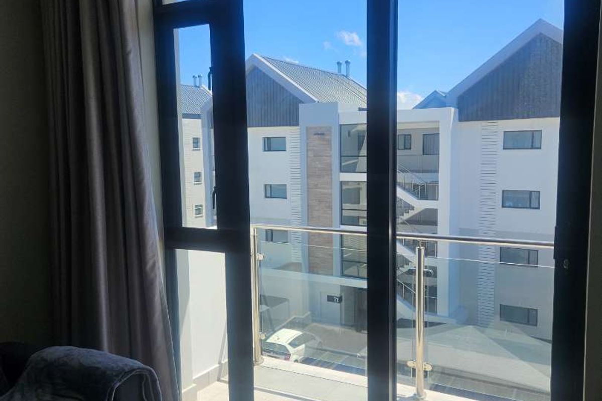 A bright living area featuring floor-to-ceiling sliding glass doors that open onto a balcony with a glass balustrade and modern tiled flooring.