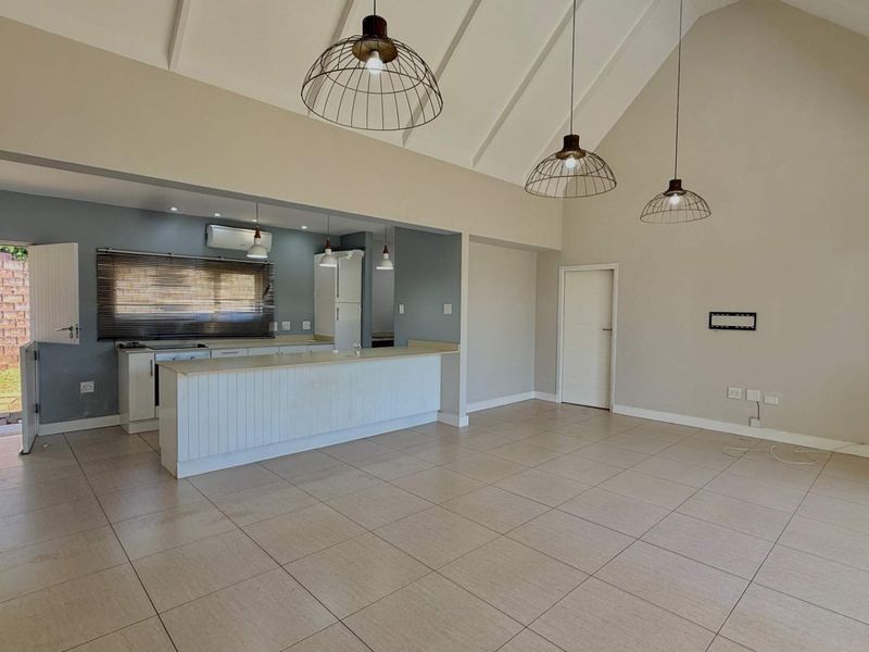 Spacious open-plan living and kitchen area featuring a high vaulted ceiling, tiled flooring, modern pendant lighting, and direct access to the rear garden.