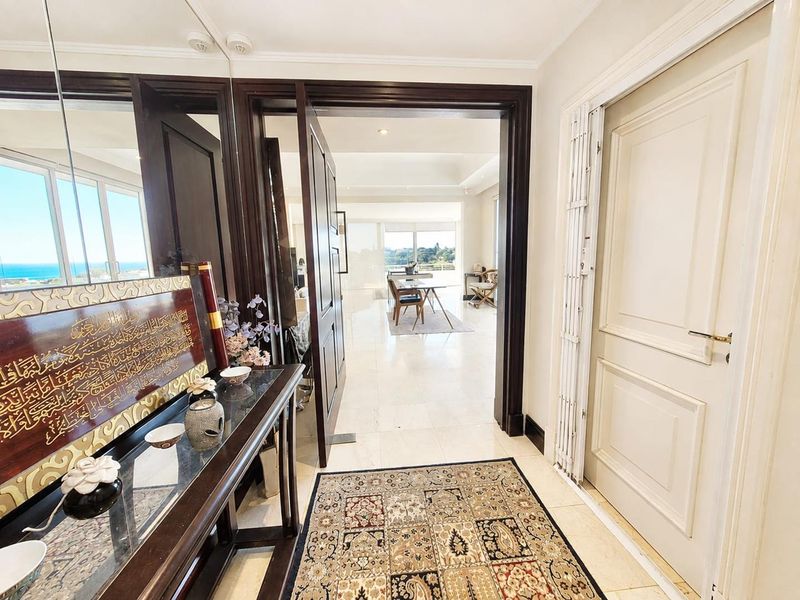 Elegant entrance foyer featuring polished marble flooring, recessed lighting, and a secure internal gate, leading into a bright, open-plan living area with ocean views.