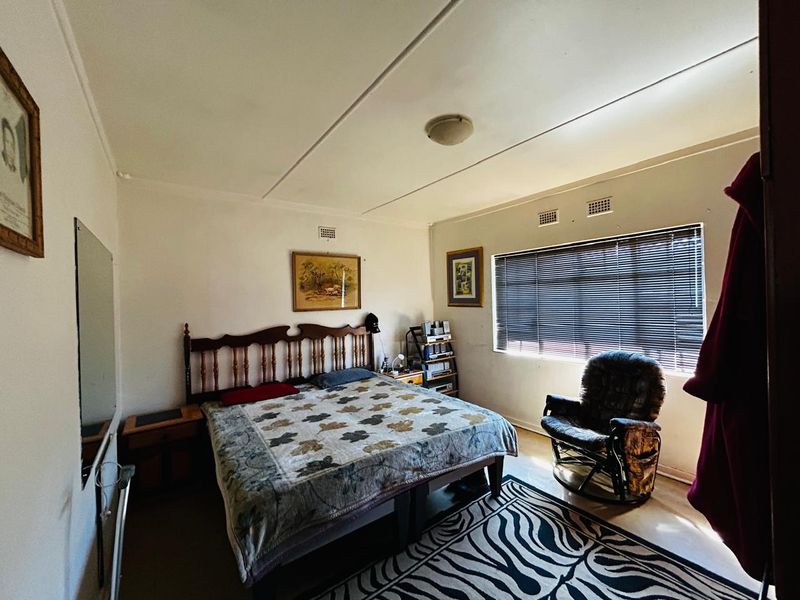 A functional bedroom featuring a window with venetian blinds and ceiling ventilation, offering a neutral space ready for updates.