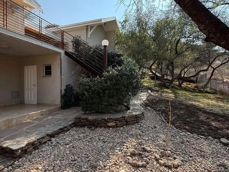Rear exterior view featuring a stone retaining wall, paved patio area, and an external metal staircase leading to the upper level.