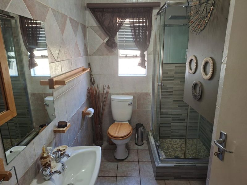 A functional bathroom featuring a shower enclosure, pedestal basin, toilet, and tiled finishes throughout.