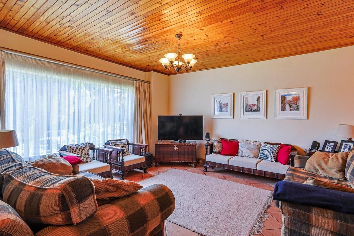 A spacious living room featuring a distinctive timber-clad vaulted ceiling, large windows with natural light, and durable tiled flooring.