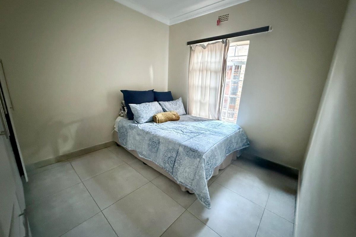 A compact bedroom featuring neutral tiled flooring, built-in cupboard space, and a window allowing natural light into the room.