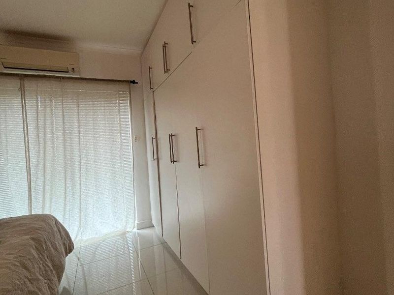 Bedroom featuring floor-to-ceiling built-in cupboards, tiled flooring, and a wall-mounted air conditioning unit.