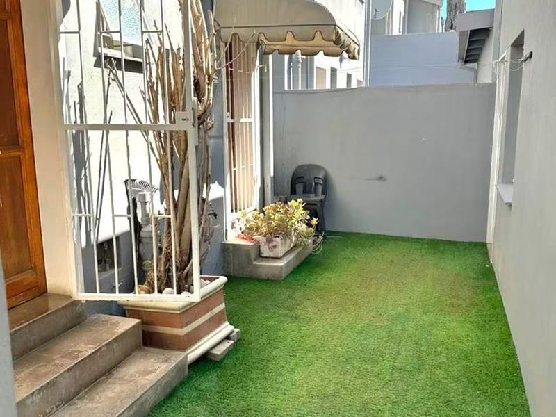 A private rear courtyard featuring artificial grass, concrete steps, and retractable awnings providing shade to the building entrance.