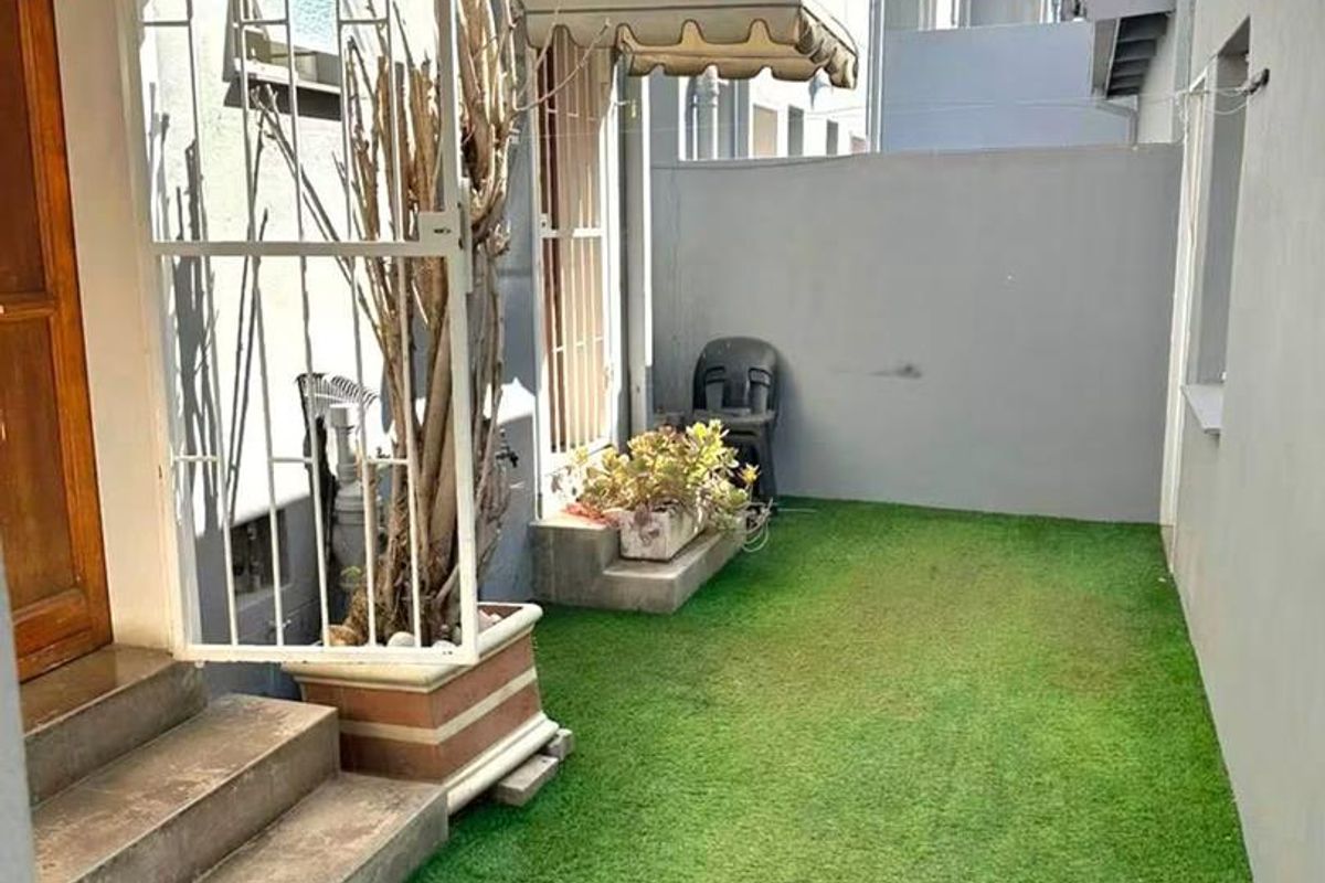 A private rear courtyard featuring artificial grass, concrete steps, and retractable awnings providing shade to the building entrance.