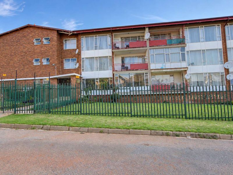 Front elevation of a multi-story apartment building featuring brick construction, private balconies, and secure perimeter fencing.