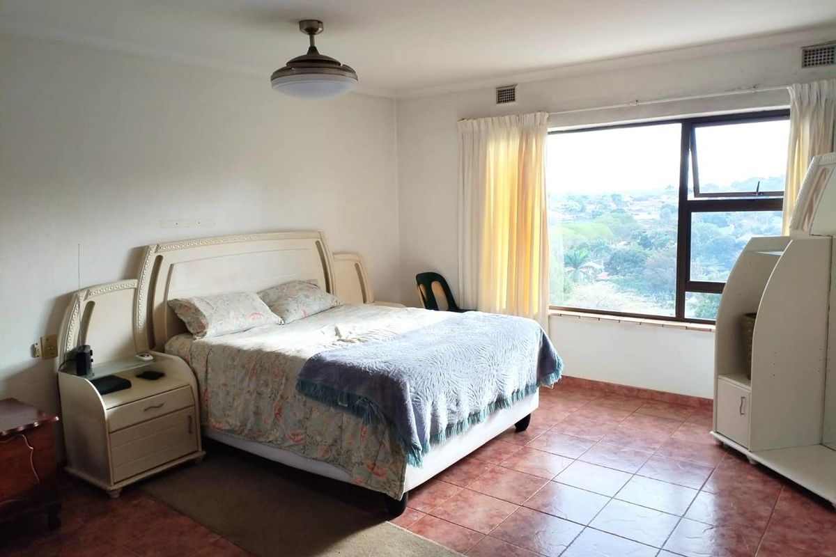 A spacious bedroom featuring tiled flooring, a ceiling fan, and a large window offering an elevated view of the surrounding area.