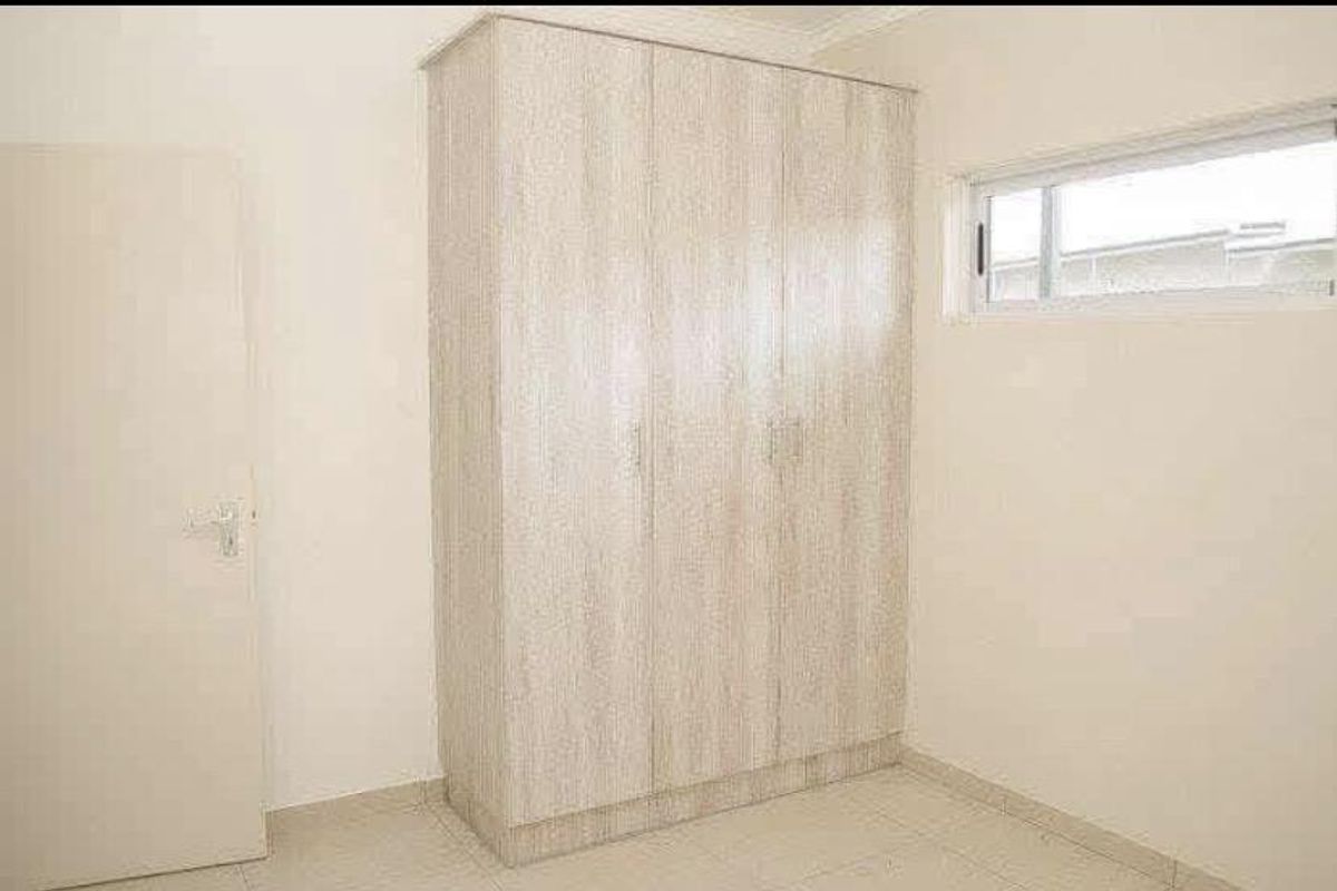 A clean, empty bedroom featuring neutral tiled flooring, a modern built-in wardrobe with wood-grain finish, and a horizontal sliding window.