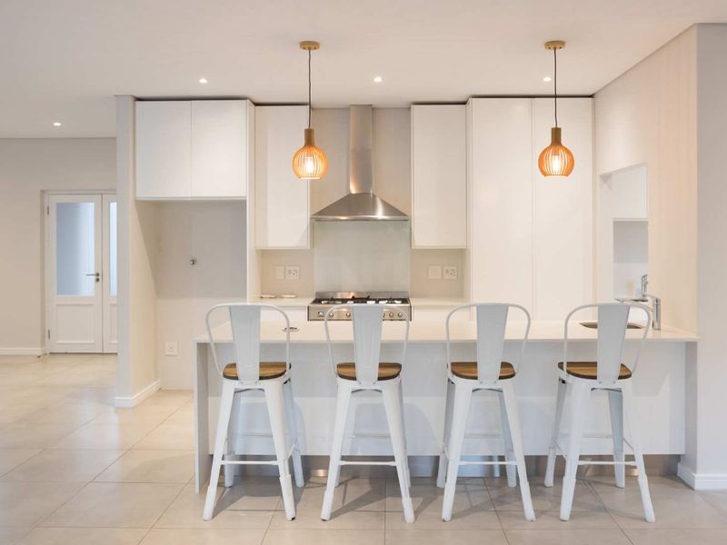 Modern kitchen featuring sleek white cabinetry, stone countertops, a gas hob with stainless steel extractor, and a breakfast bar with pendant lighting.