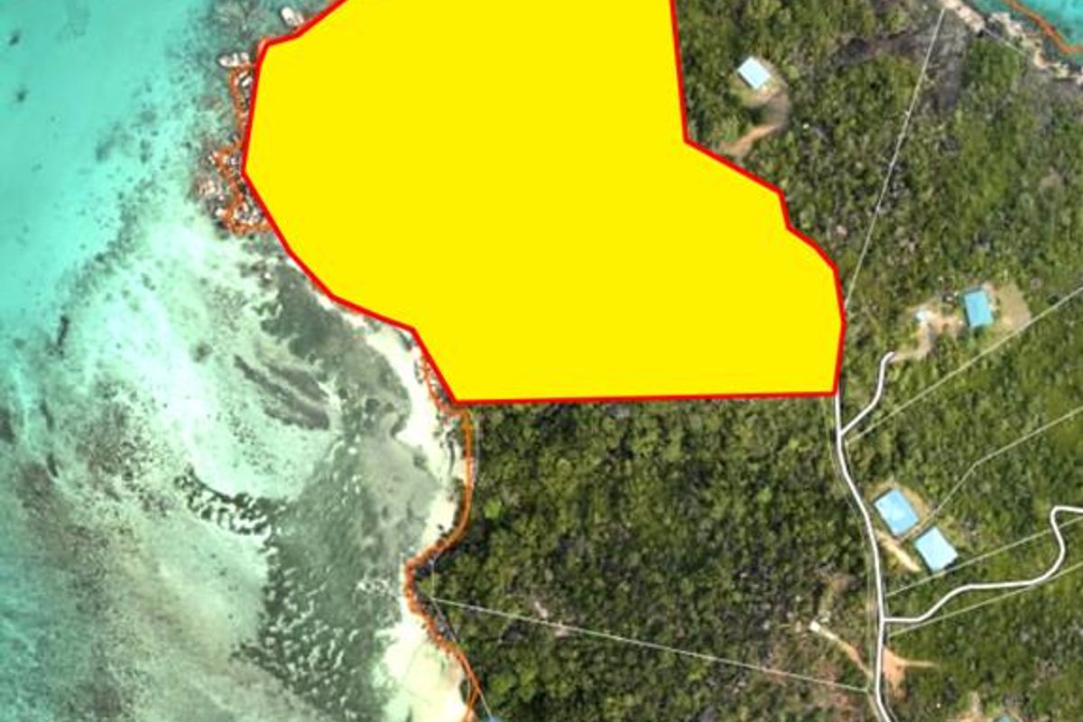 Aerial view of a coastal residential land plot highlighted in yellow, featuring direct ocean access and surrounding tropical vegetation.