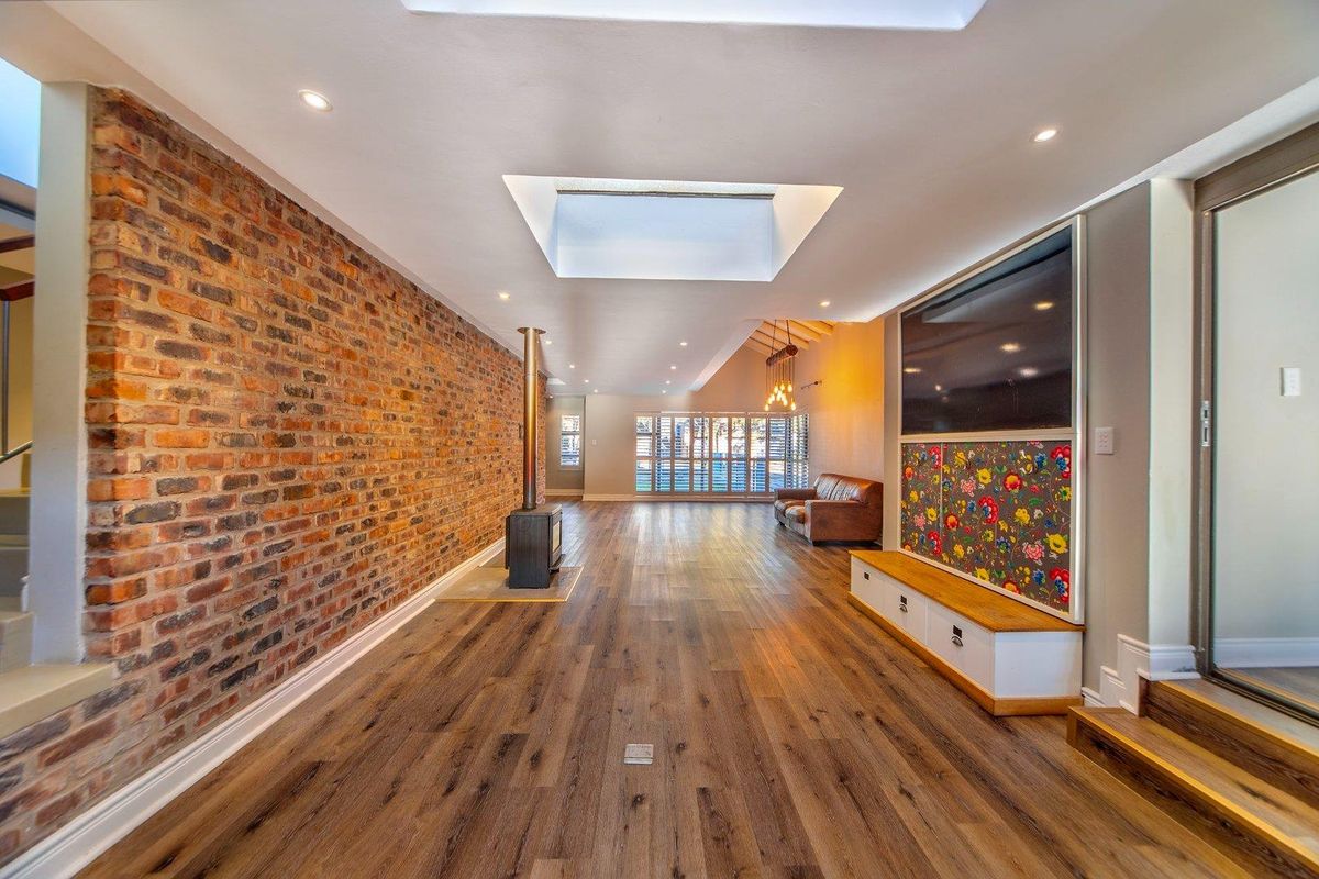 Spacious living area featuring exposed brick wall, wood-burning fireplace, skylights, and modern wood-look flooring with integrated cabinetry.