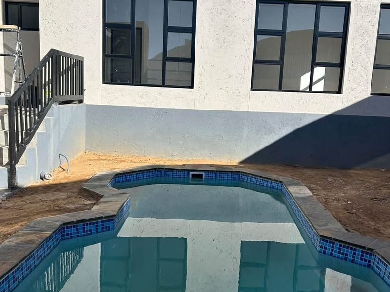 A backyard pool area featuring a swimming pool with tiled coping, adjacent to a building exterior with aluminium windows and a metal staircase.