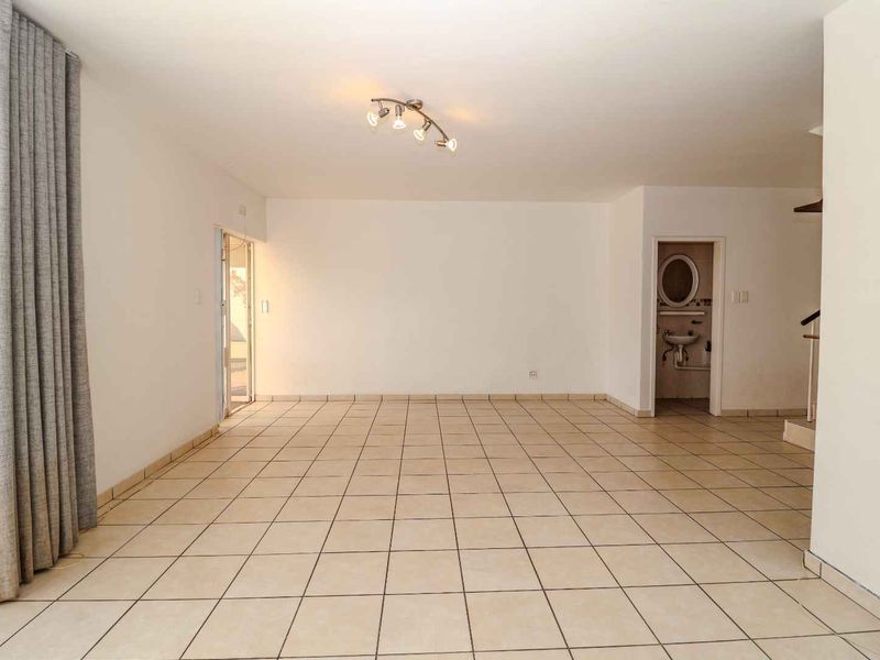 A spacious, empty living area featuring neutral tiled flooring and direct access to an outdoor space, offering a blank canvas for interior design.