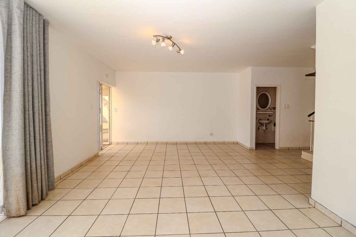 A spacious, empty living area featuring neutral tiled flooring and direct access to an outdoor space, offering a blank canvas for interior design.