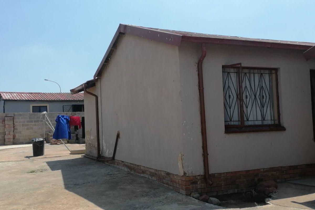 Rear exterior view of the property showing concrete driveway, perimeter wall, and building facade with security bars on windows.