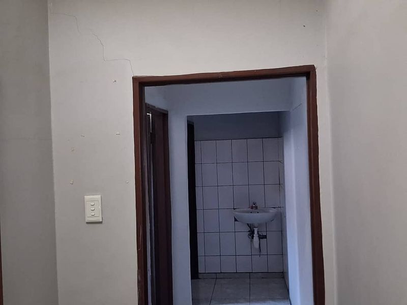 A view of a hallway leading to a small washroom area featuring a wall-mounted basin and tiled splashback.