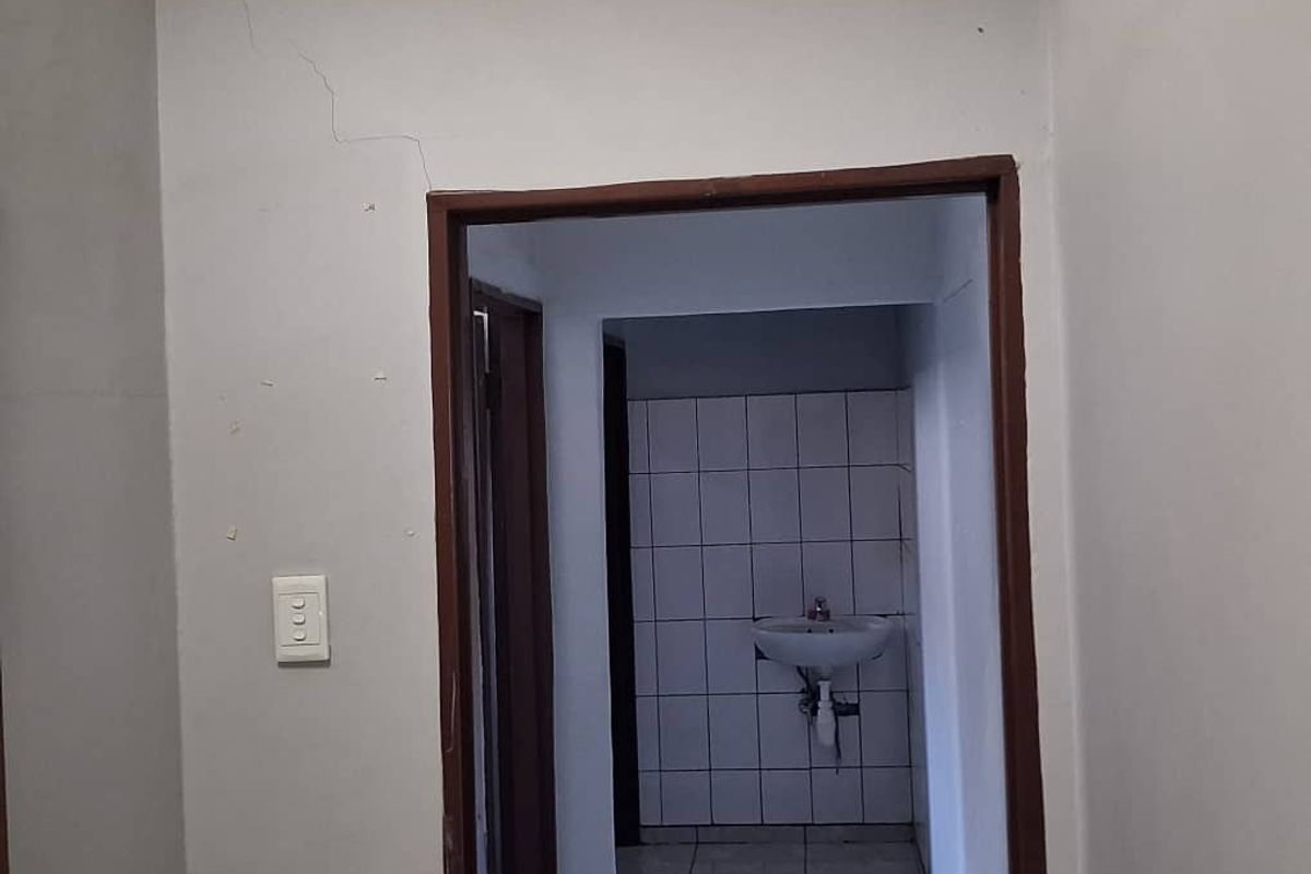 A view of a hallway leading to a small washroom area featuring a wall-mounted basin and tiled splashback.