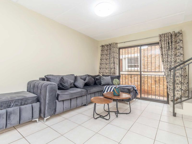 A living room featuring tiled flooring, a sliding glass door with security gate, and an adjacent staircase with a metal railing.