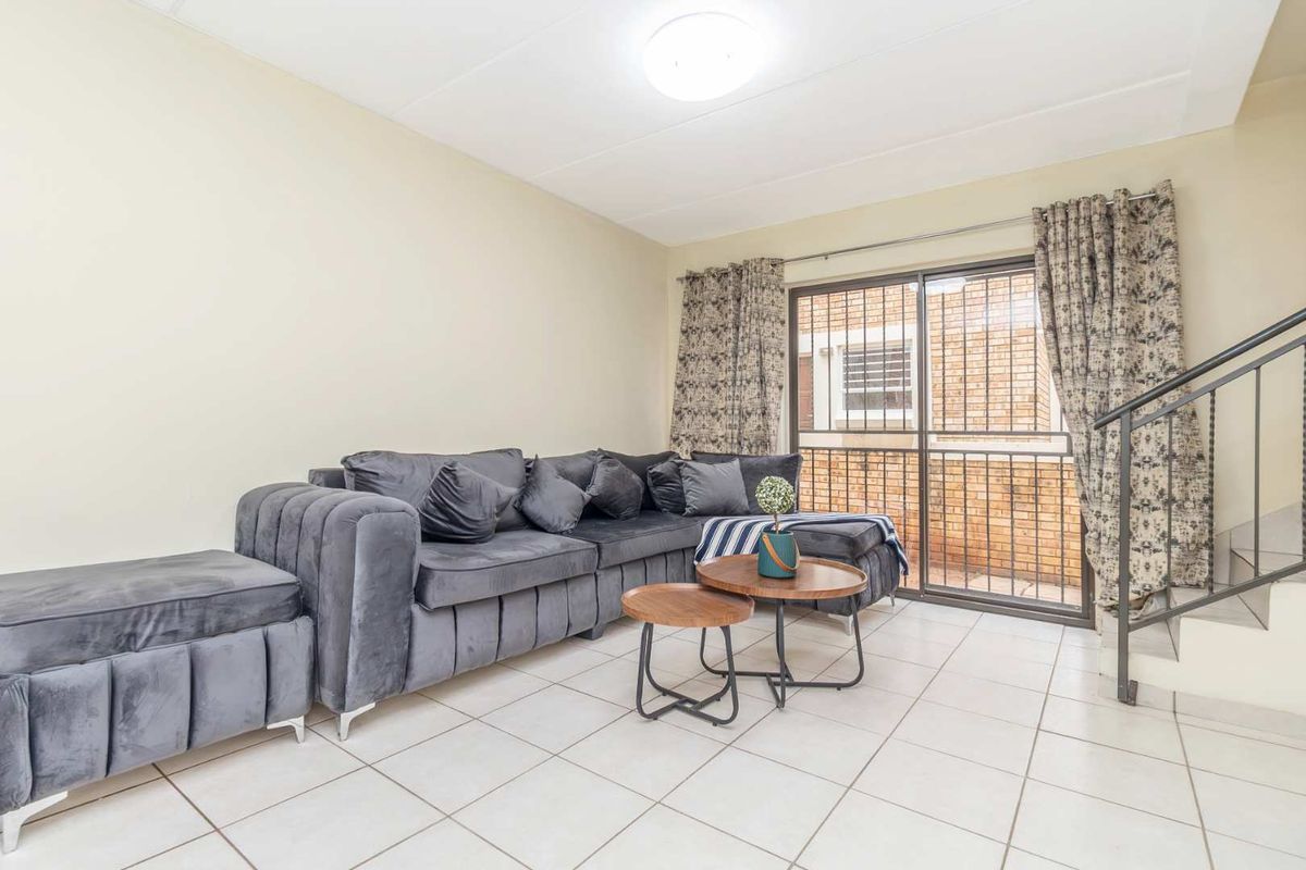 A living room featuring tiled flooring, a sliding glass door with security gate, and an adjacent staircase with a metal railing.