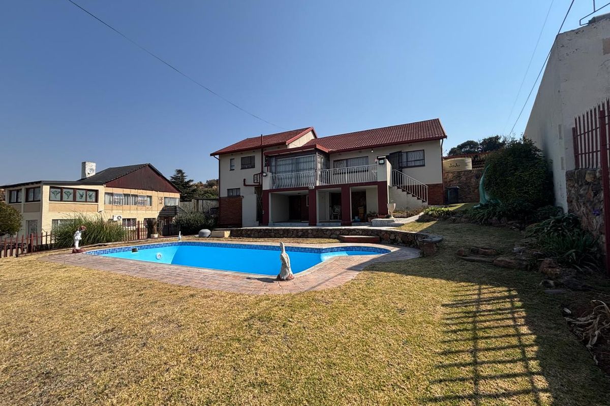 Rear view of a two-story house featuring a swimming pool, paved surround, elevated balcony, and a water tank set within a garden area.