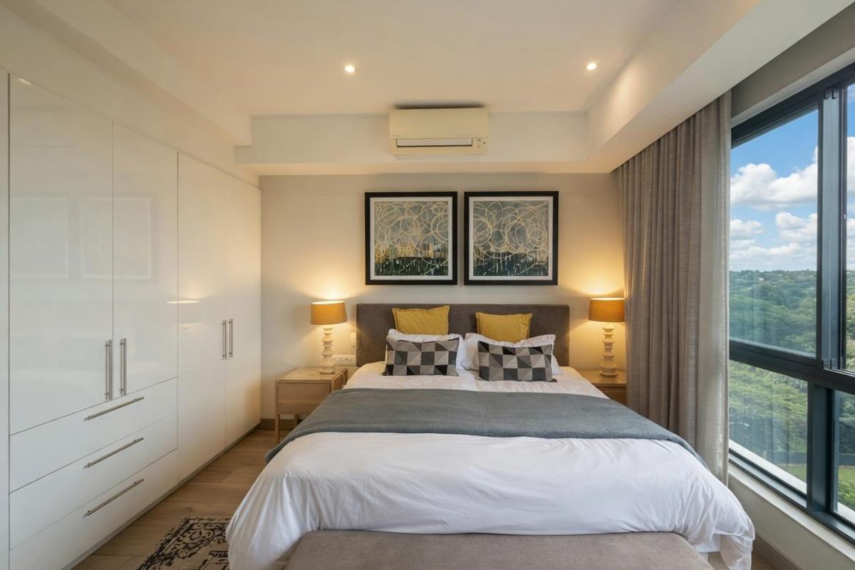 A modern, well-maintained bedroom featuring built-in floor-to-ceiling wardrobes, recessed downlighting, a wall-mounted air conditioning unit, and large windows offering expansive views.