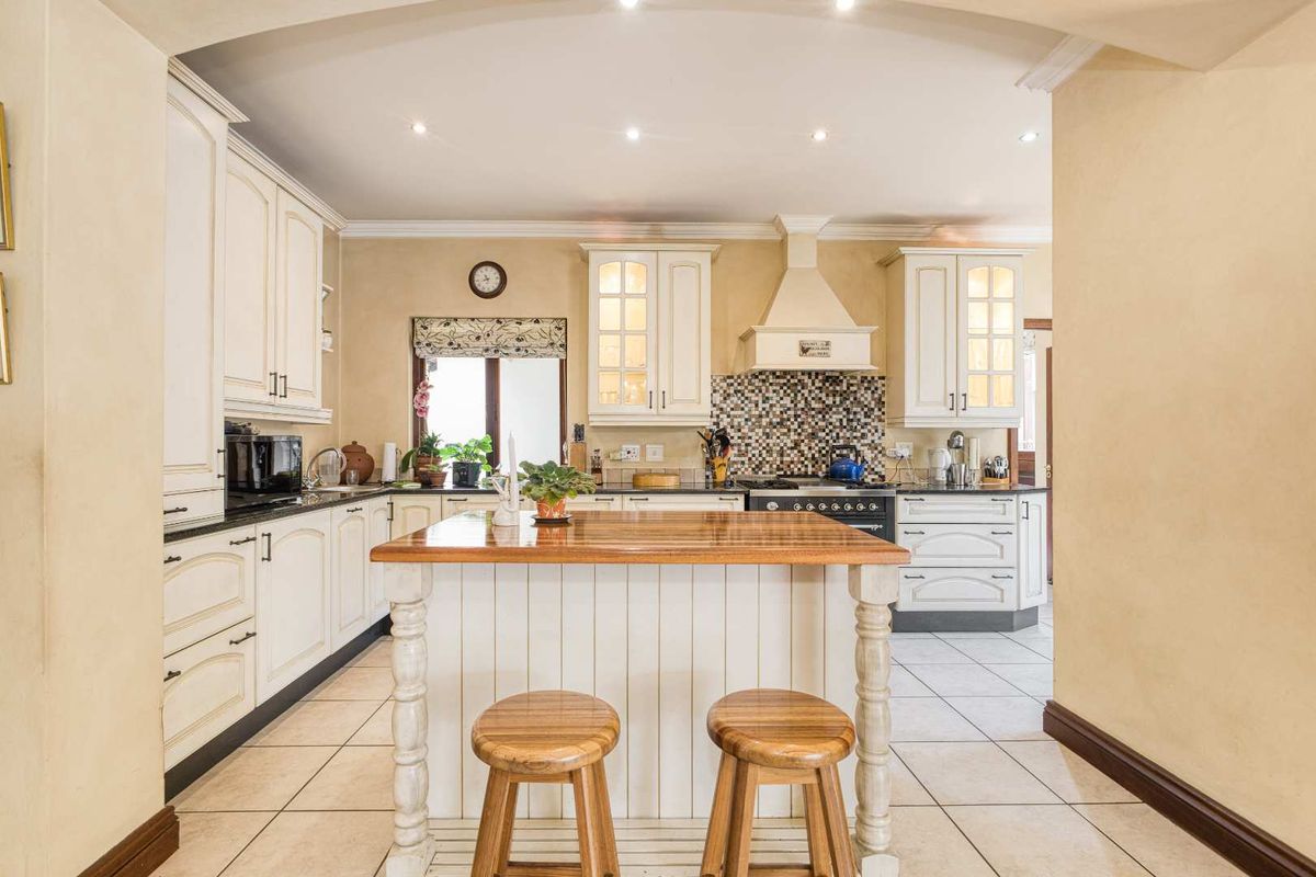 A classic kitchen featuring cream cabinetry, a central wooden island, tiled flooring, and a mosaic tile backsplash with a built-in extractor fan.