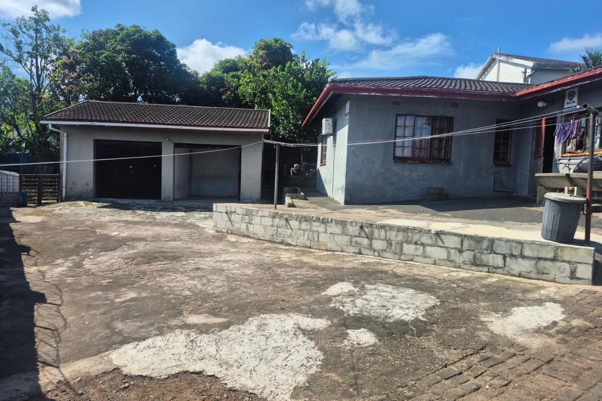 Rear exterior view of the property featuring a detached garage, concrete driveway, and a low retaining wall.