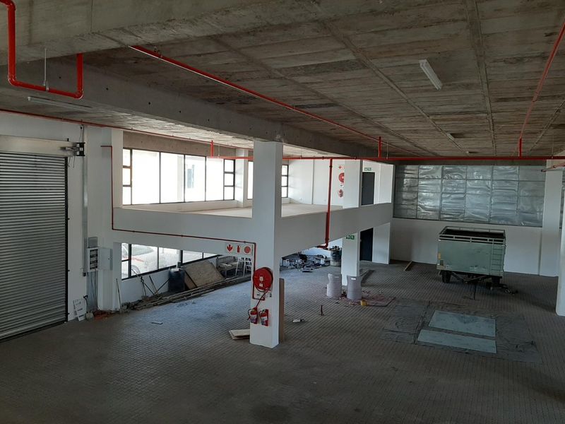 Spacious industrial utility area featuring a mezzanine level, exposed concrete ceilings, fire sprinkler system, and a large roller shutter door for easy access.