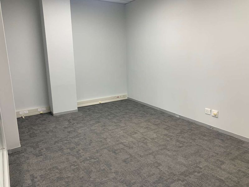 A vacant, neutral-toned office space featuring grey carpet tiles, integrated electrical and data connectivity, and a clean, professional layout.