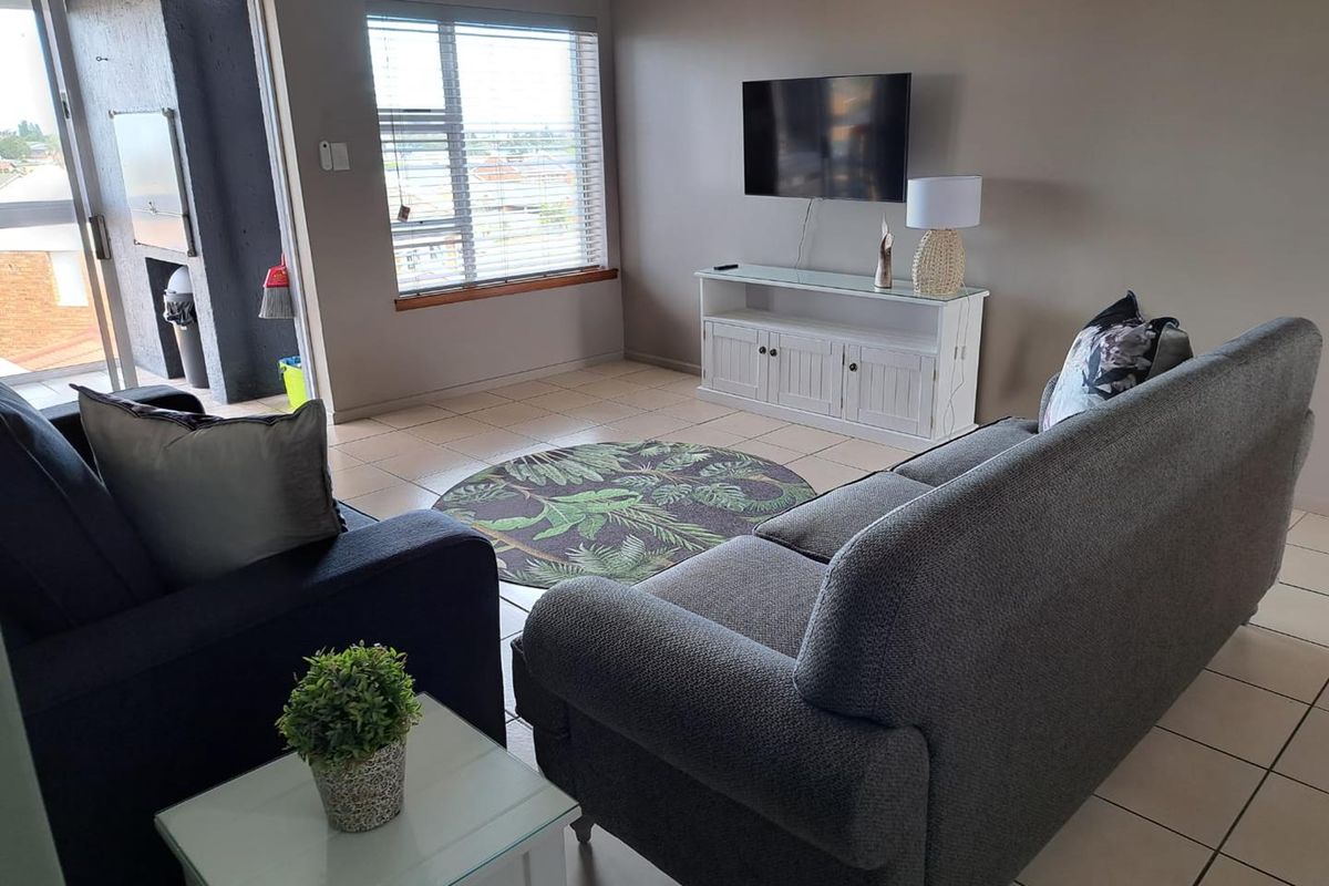 A bright living room featuring tiled flooring, large windows with blinds, and direct access to an outdoor balcony area.