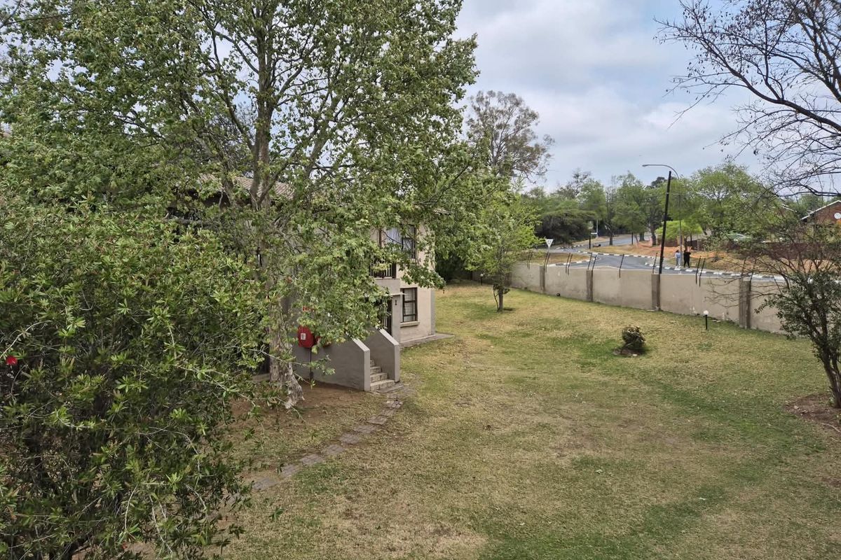 An elevated view of the apartment complex grounds featuring a lawn, mature trees, and a perimeter boundary wall.