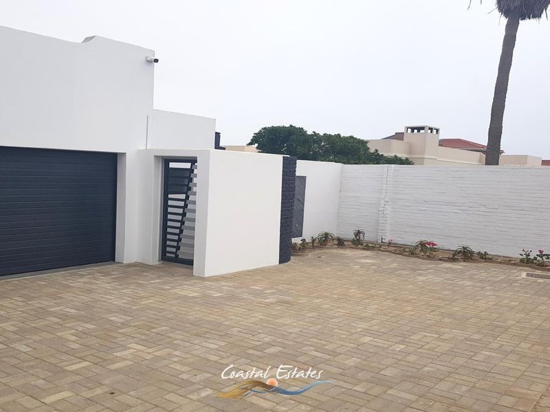 Front exterior view featuring a paved driveway, modern garage door, secure pedestrian gate, and a clean white boundary wall.