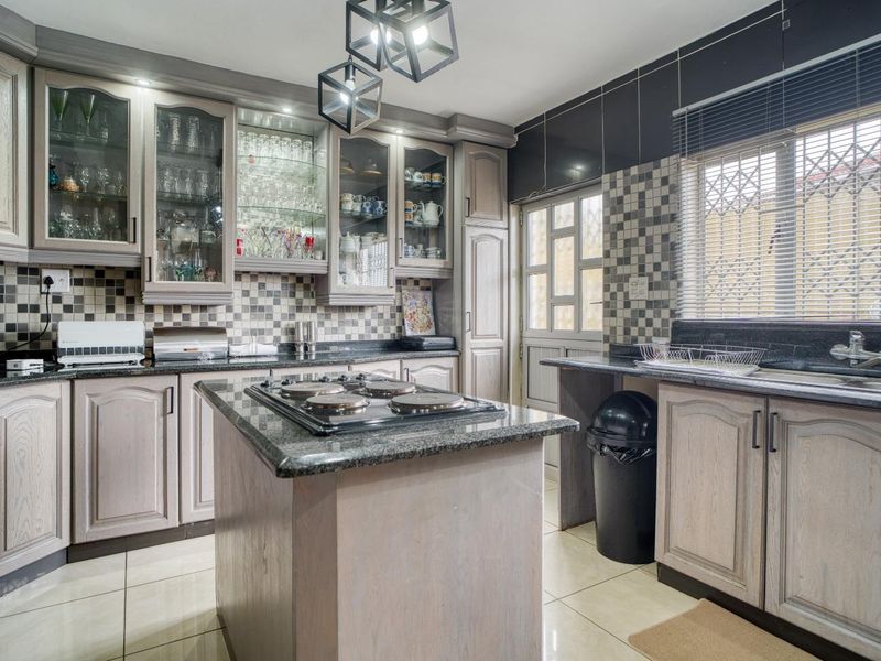 A well-appointed kitchen featuring granite countertops, a central island with a built-in hob, glass-front cabinetry, and a decorative tiled backsplash.