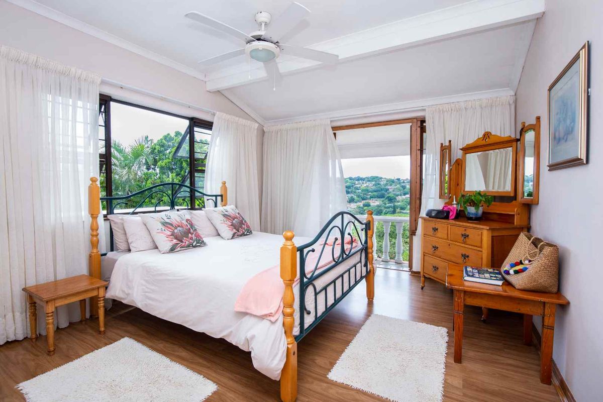 A bright bedroom featuring laminate flooring, a ceiling fan, and direct access to a balcony with scenic views.