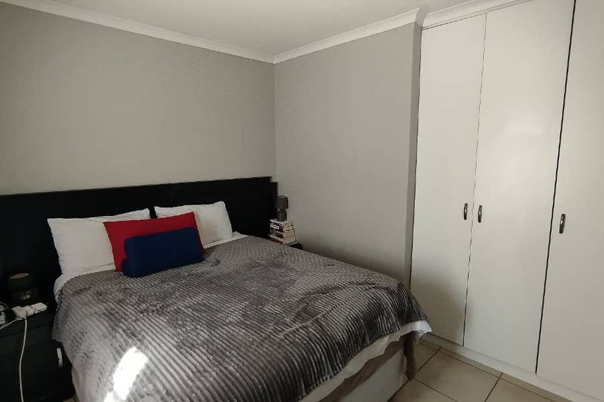 A well-maintained bedroom featuring neutral wall tones, tiled flooring, and ample built-in cupboard storage.