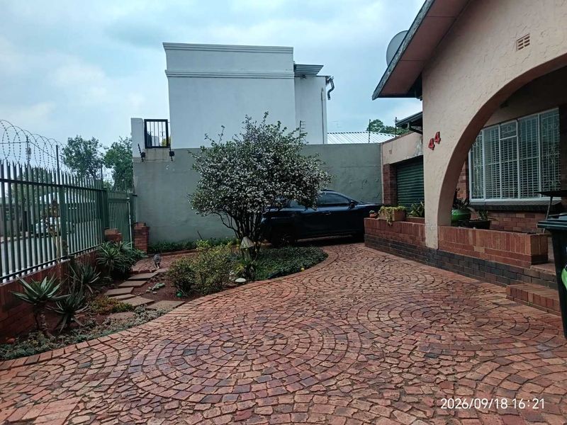 Front exterior view of the property featuring a circular brick paved driveway, security fencing, and an arched entrance.