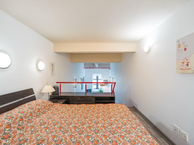 A mezzanine bedroom area featuring laminate flooring, wall-mounted lighting, and a red metal safety balustrade overlooking the lower level.