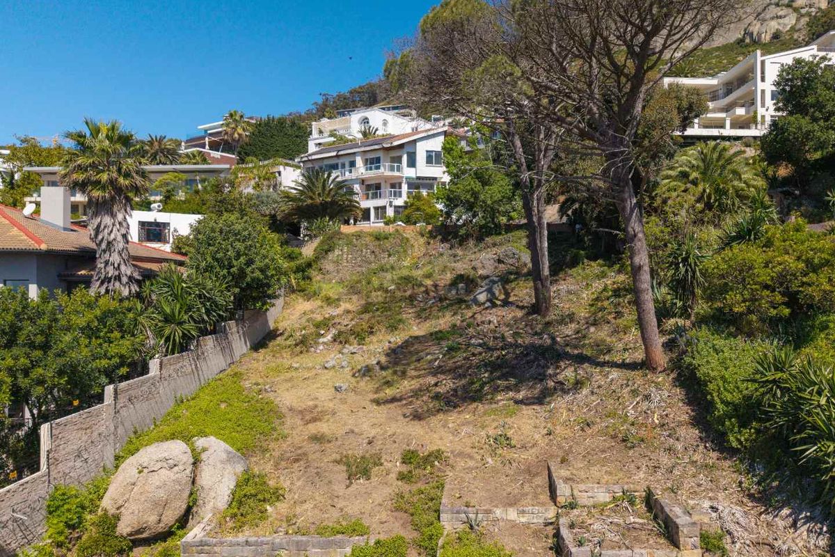 A sloped residential vacant land plot featuring established trees, stone retaining walls, and boundary fencing in a hillside neighborhood setting.