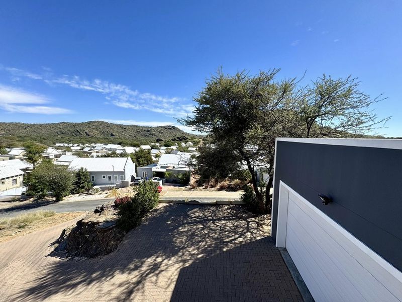 Elevated view of the property frontage featuring a paved driveway, modern garage door, and surrounding neighbourhood landscape.