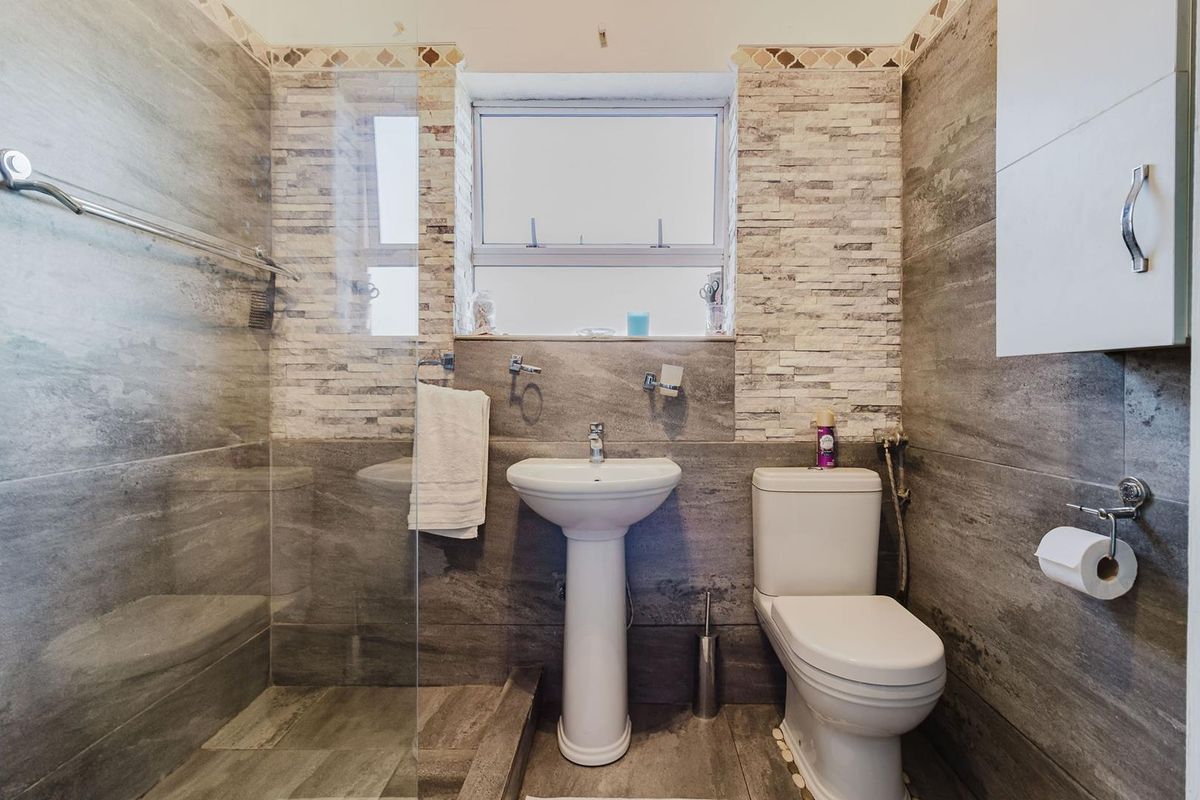 Modern bathroom featuring grey stone-look wall and floor tiles, a pedestal sink, toilet, and a glass-enclosed shower area.