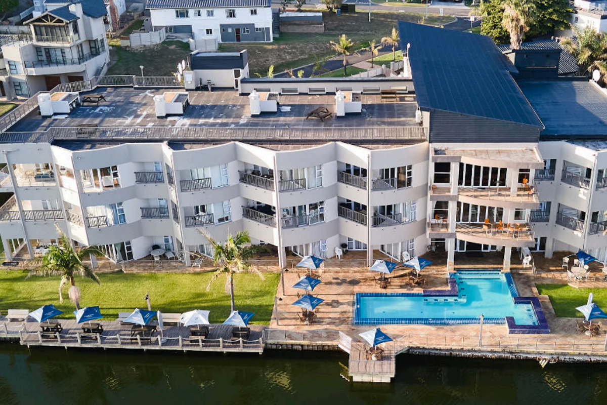 Aerial view of a multi-story apartment complex featuring balconies, a swimming pool, and direct waterfront access with landscaped grounds.