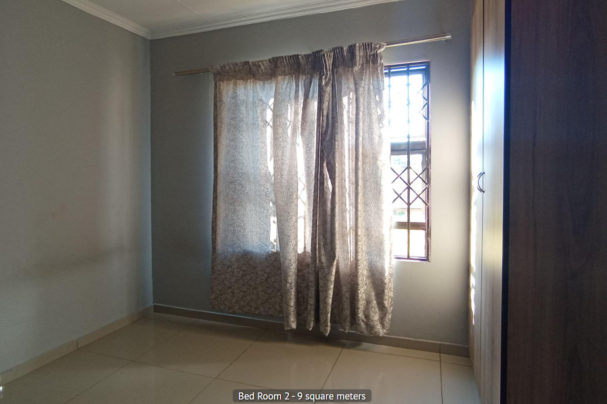 A bedroom featuring tiled flooring, a built-in wardrobe, and a window fitted with security bars.
