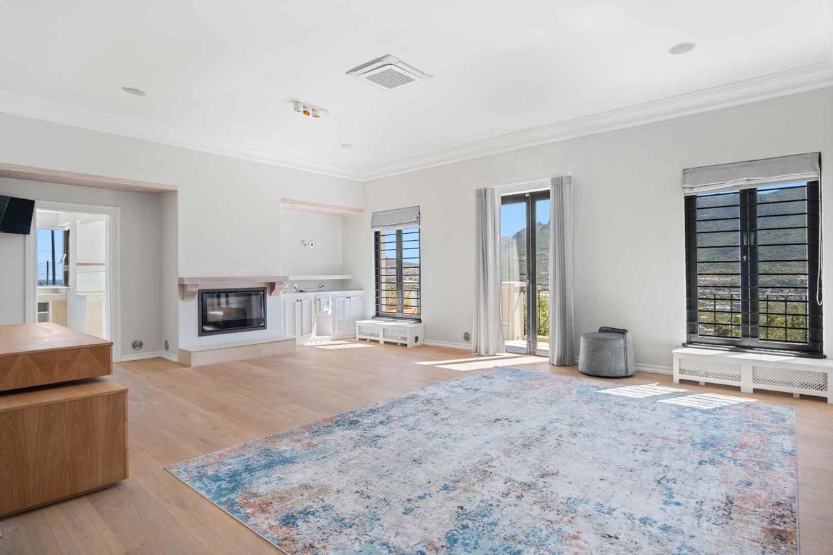 Spacious living room featuring timber flooring, a built-in fireplace, custom cabinetry, and large windows with security bars, offering bright and airy living space.