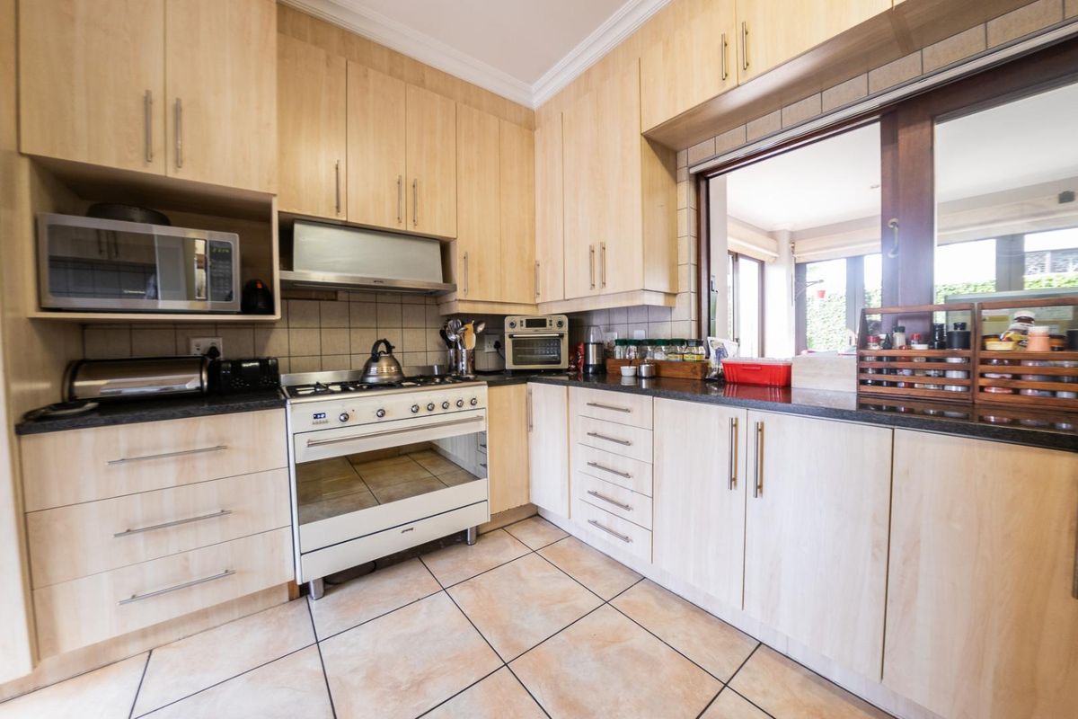 A functional kitchen featuring light wood-toned cabinetry, dark granite countertops, a built-in oven with gas hob, and tiled flooring.