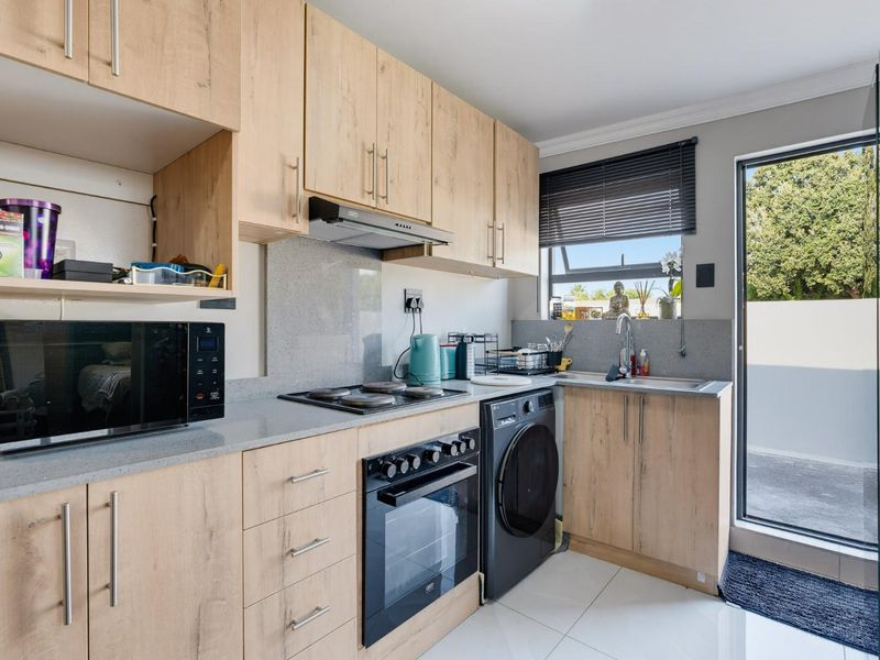 Modern kitchen featuring light wood-finish cabinetry, stone countertops, integrated oven and hob, and direct access to an outdoor area.