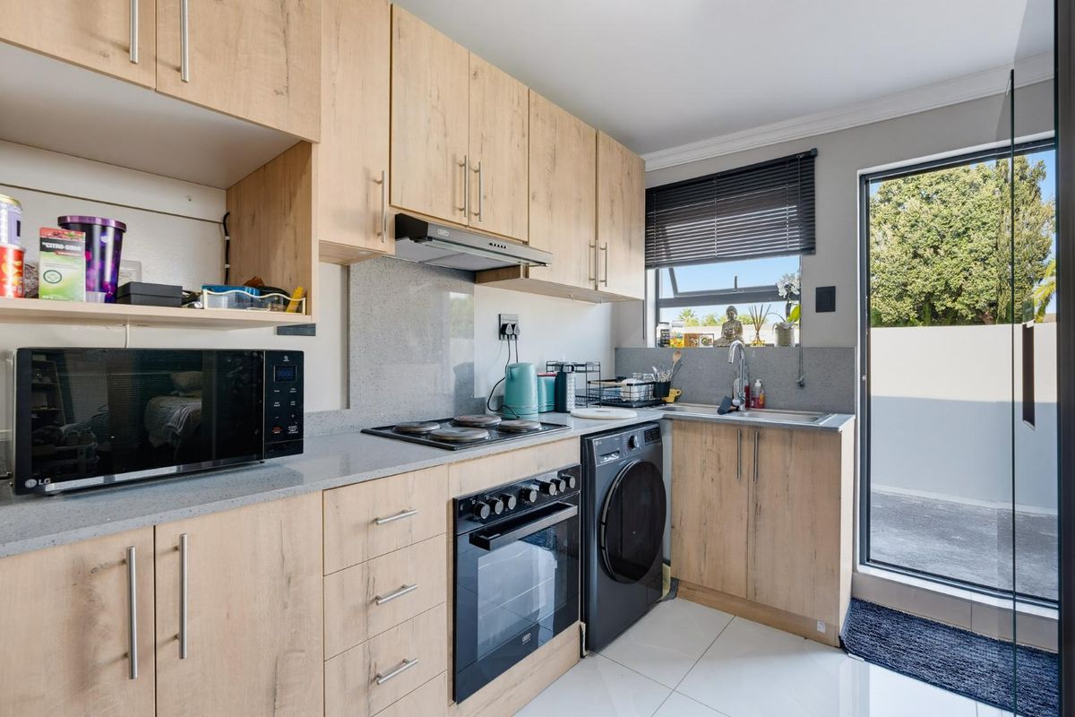 Modern kitchen featuring light wood-finish cabinetry, stone countertops, integrated oven and hob, and direct access to an outdoor area.
